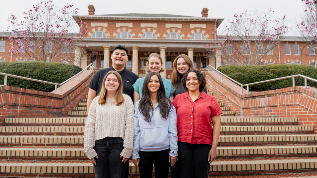 Photograph of Pack Assessment Ambassadors standing on the stairs in front of the 1911 Building. There are three students standing on two rows. Everyone is smiling.